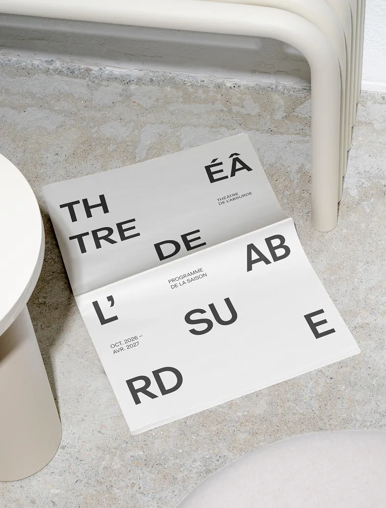 Newspaper on floor with bold black text: Théâtre de l'Absurde program for Oct 2026 to Apr 2027.