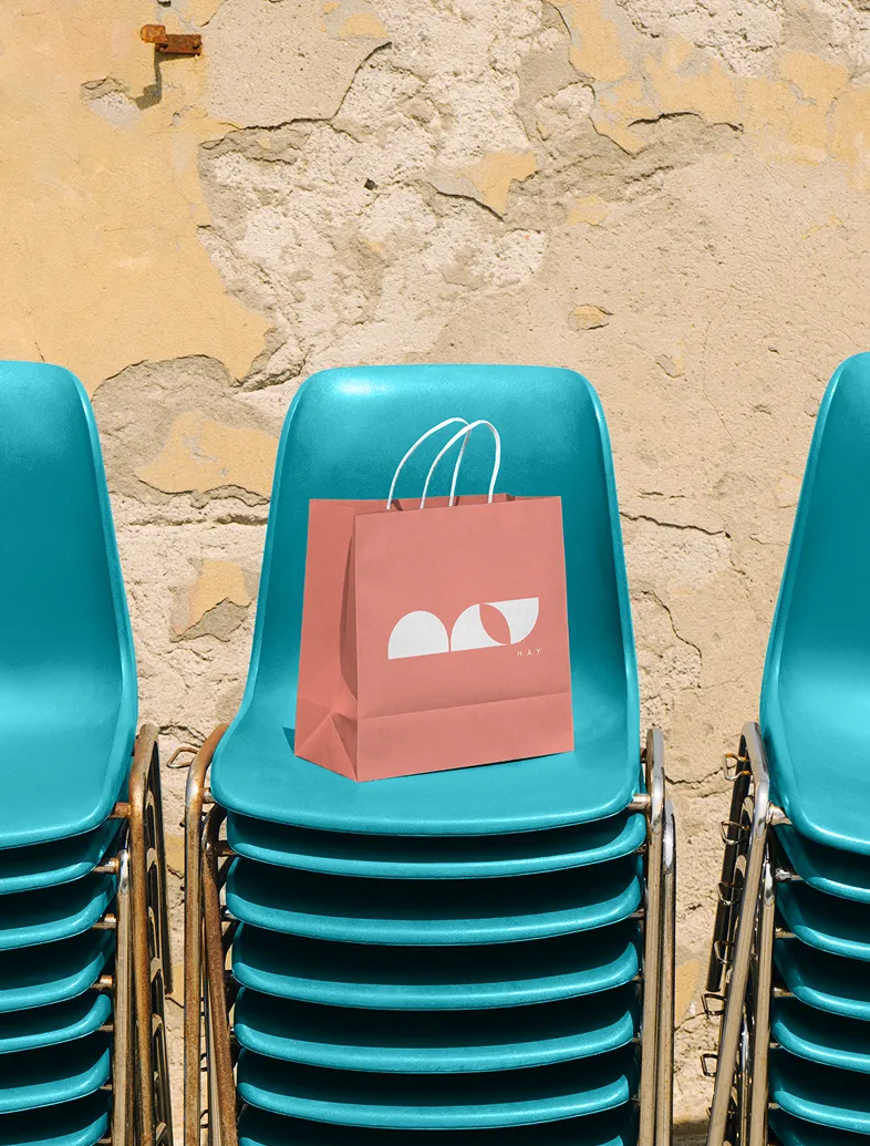 Stack of teal plastic chairs with a pink shopping bag on top against a cracked beige wall.