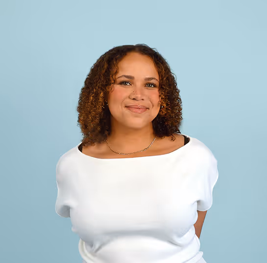 Smiling woman with curly hair wearing a white top against a light blue background.