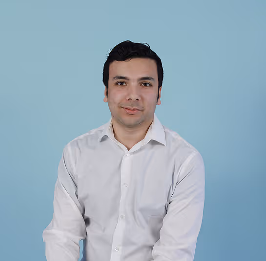 Man with short black hair wearing a white button-up shirt, sitting against a light blue background.
