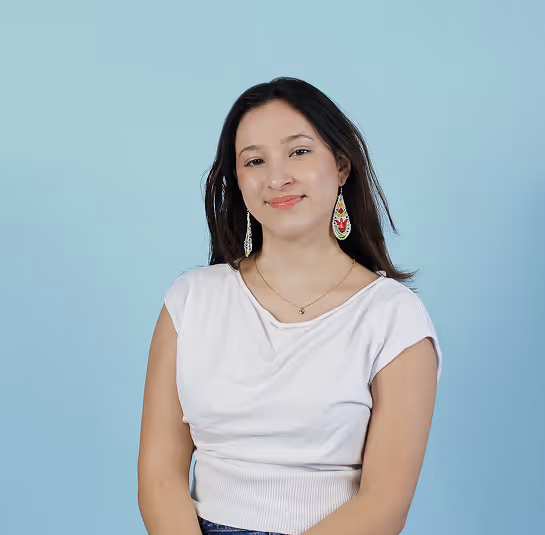 Smiling woman with long dark hair wearing white top and colorful dangling earrings on blue background.