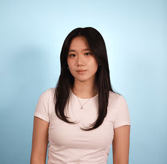 Young woman with long dark hair wearing a white shirt and necklace against a light blue background.