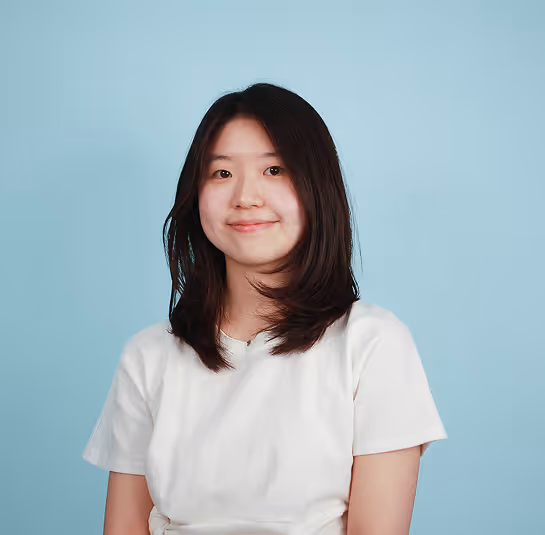 Young woman with shoulder-length black hair wearing a white t-shirt against a light blue background.