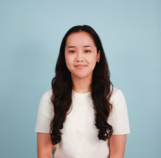 Woman with long curly hair wearing a white buttoned shirt against a light blue background.