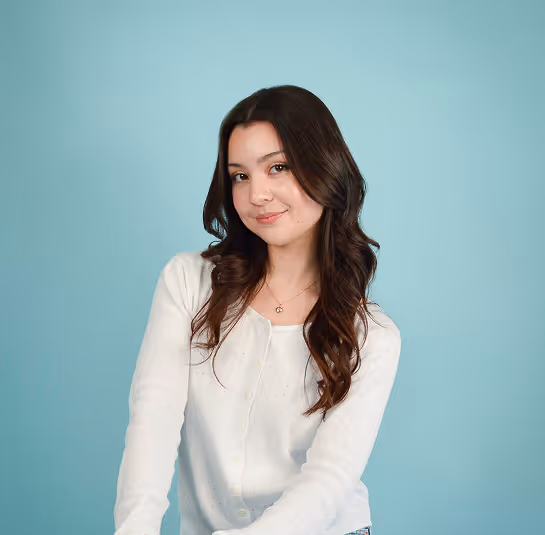 Young woman with long dark hair wearing a white buttoned cardigan against a light blue background.