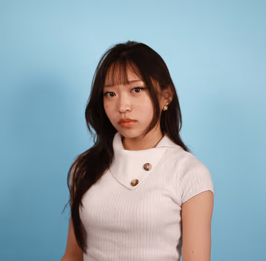 Young woman with long dark hair wearing white knit top against a light blue background.