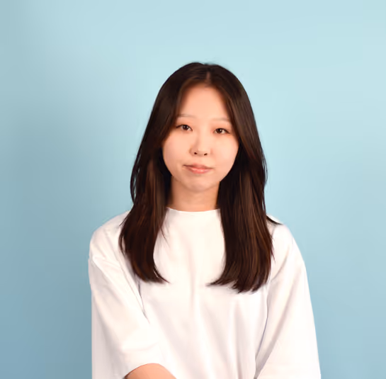 Young woman with long dark hair wearing a white shirt against a plain light blue background.