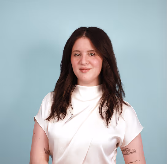 Young woman with long dark hair wearing a white blouse against a light blue background.