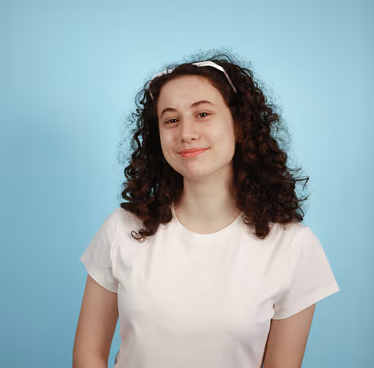 Smiling young woman with curly hair wearing a white t-shirt and headband against a blue background.