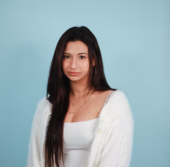 Young woman with long dark hair in a white top and fuzzy cardigan on a light blue background.