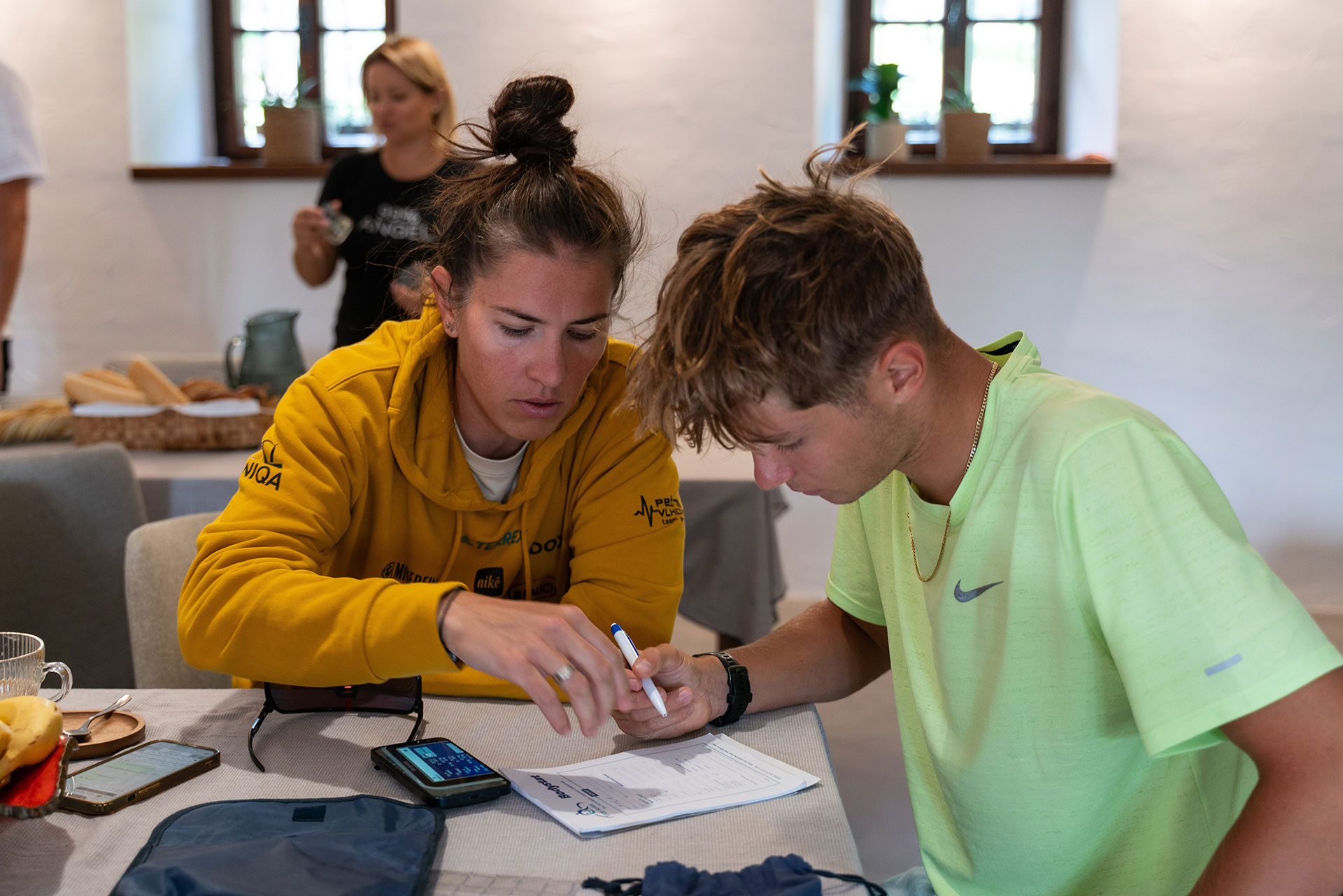 Two young people focusing on paperwork at a table in a room with white walls and windows.