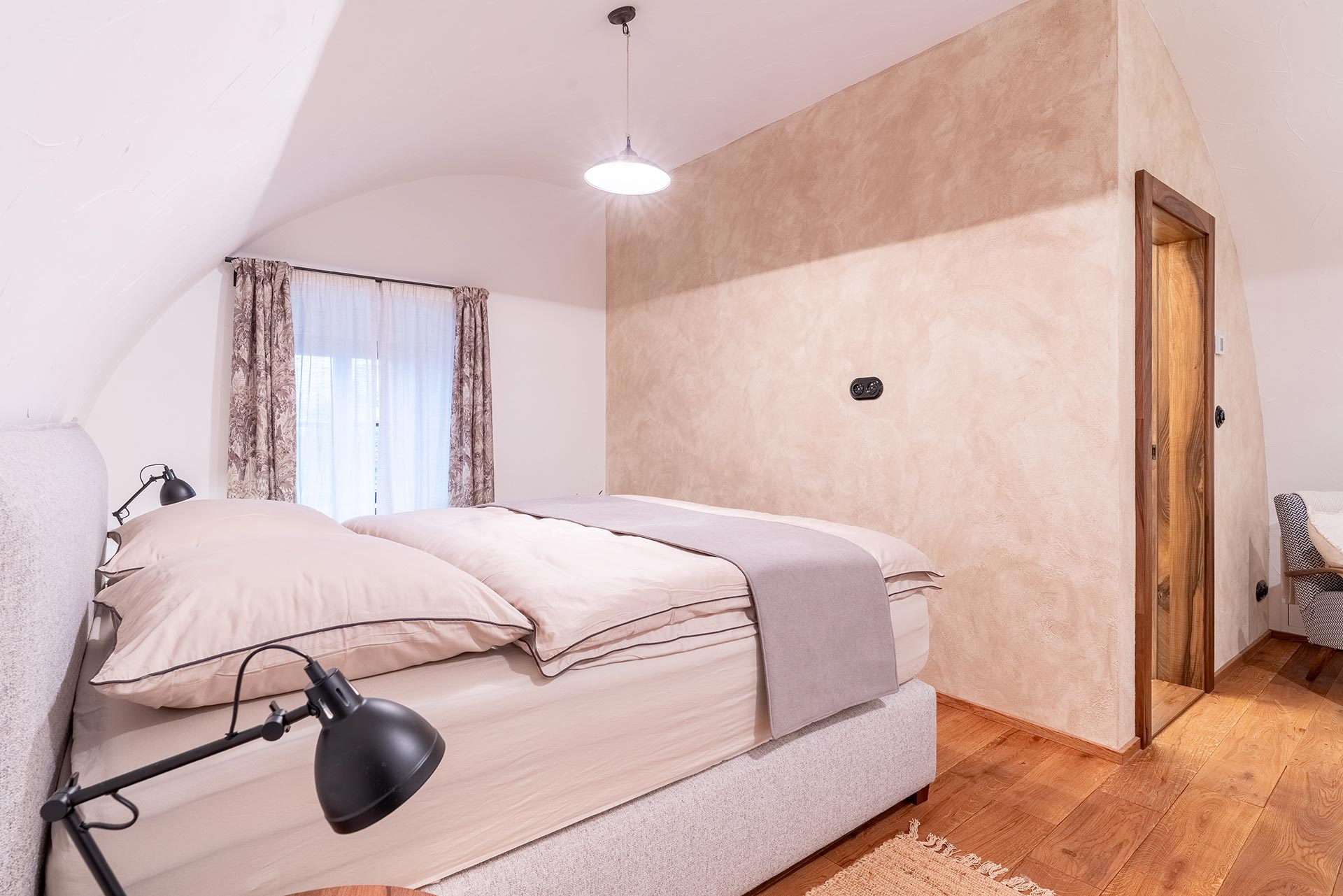 Cozy bedroom with a light gray bed, soft beige bedding, patterned curtains, and wooden floor.