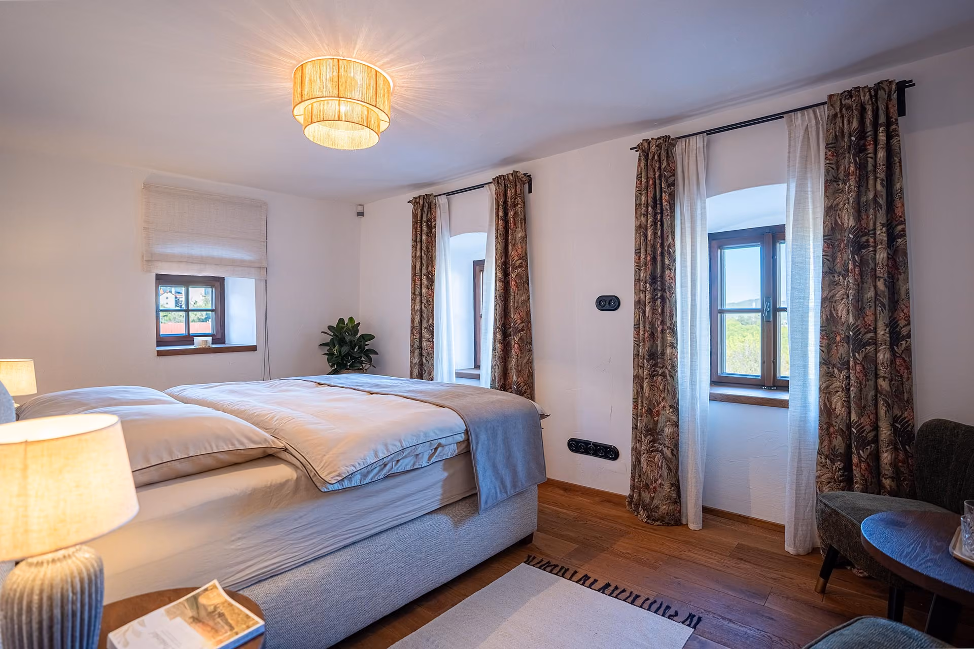 Spálňa apartmánu s manželskou posteľou, vzorovanými závesmi a dvoma oknami