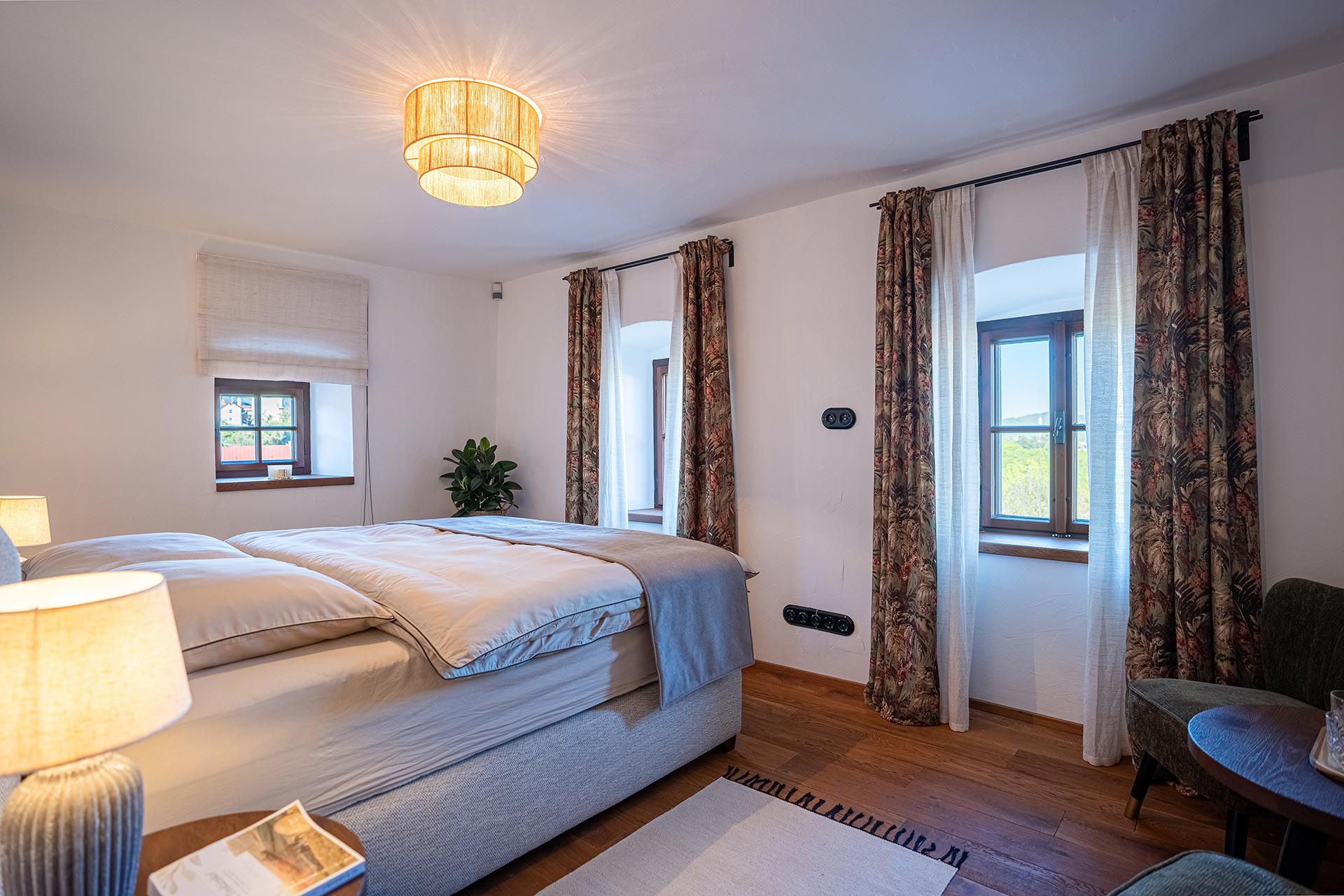 Cozy bedroom with covered bed, patterned curtains, wooden floor, and warm ceiling light