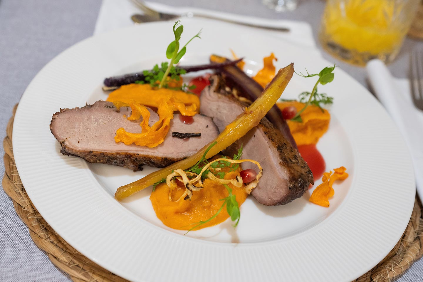 Plate with sliced roasted meat, orange puree, roasted carrots, and greens on a white plate.