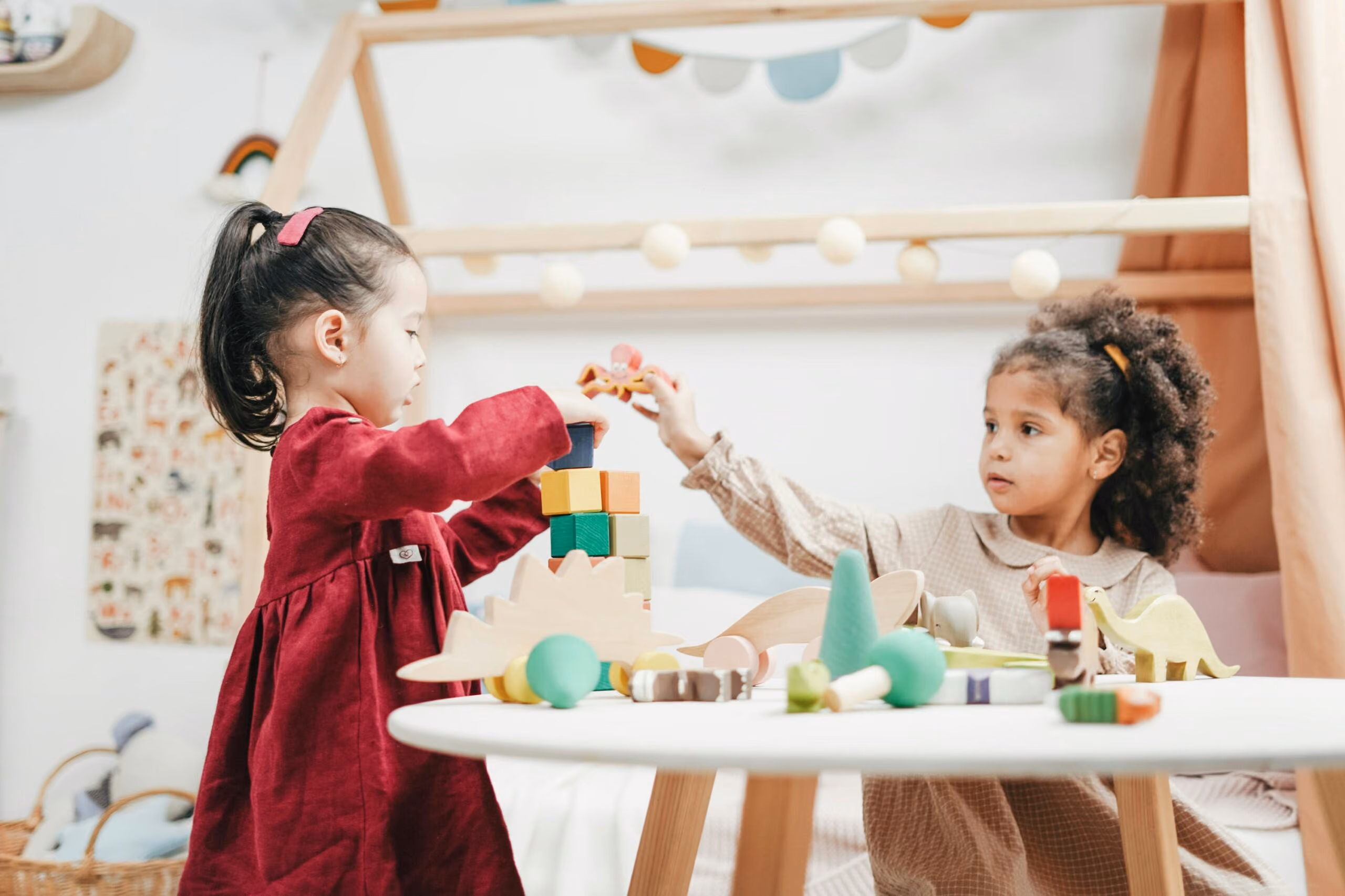 Two children build a colorful block tower together at a white table.
