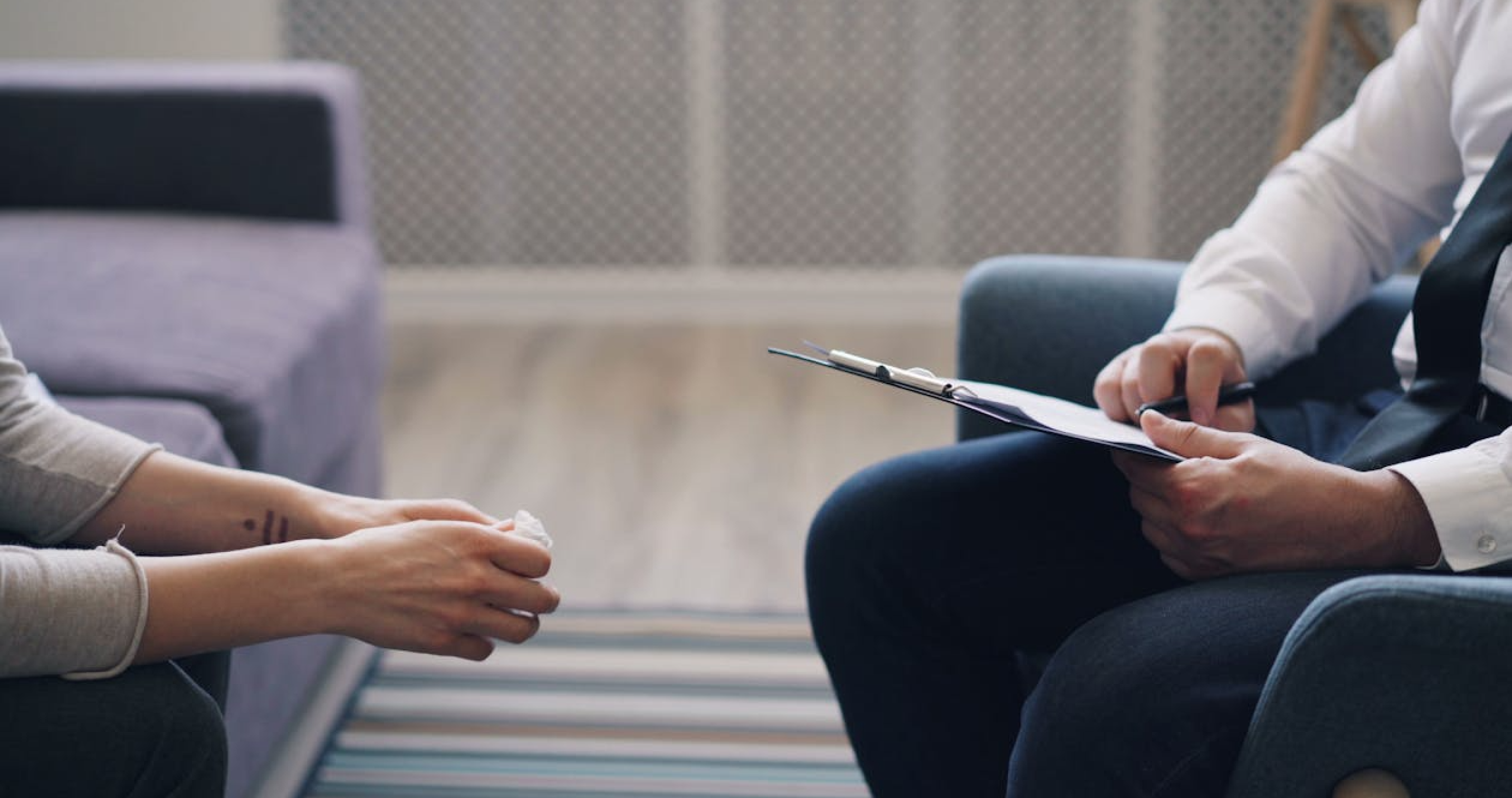 A person writes notes on a clipboard while another holds a tissue during a counseling session.