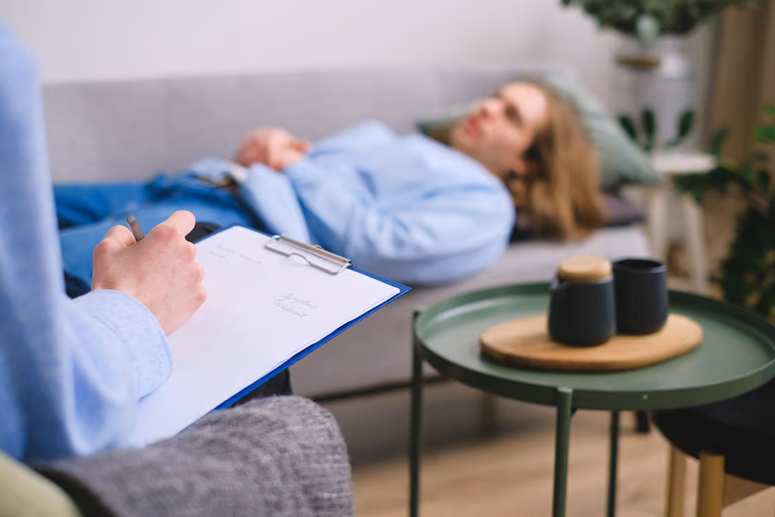 A person holds a clipboard labeled "Session Notes" while another reclines on a couch.