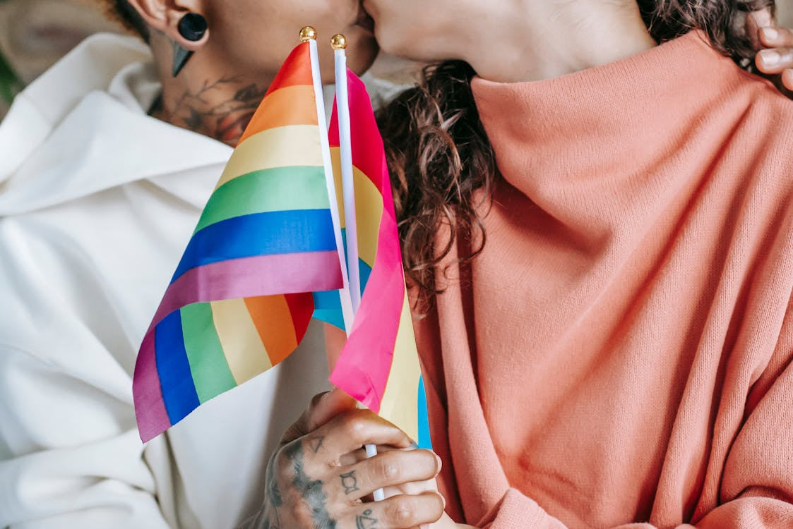 Two people kiss while holding small rainbow pride flags.