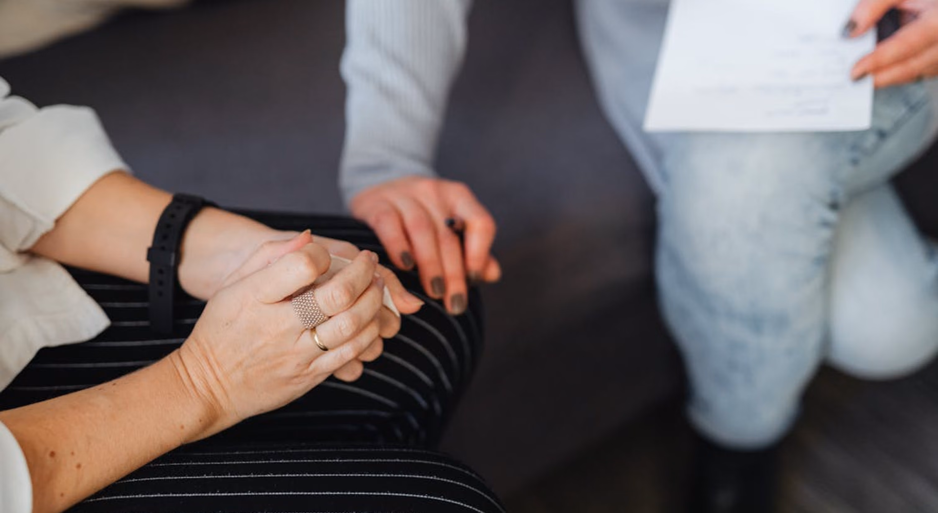 A person holds a white document while another clasps their hands.