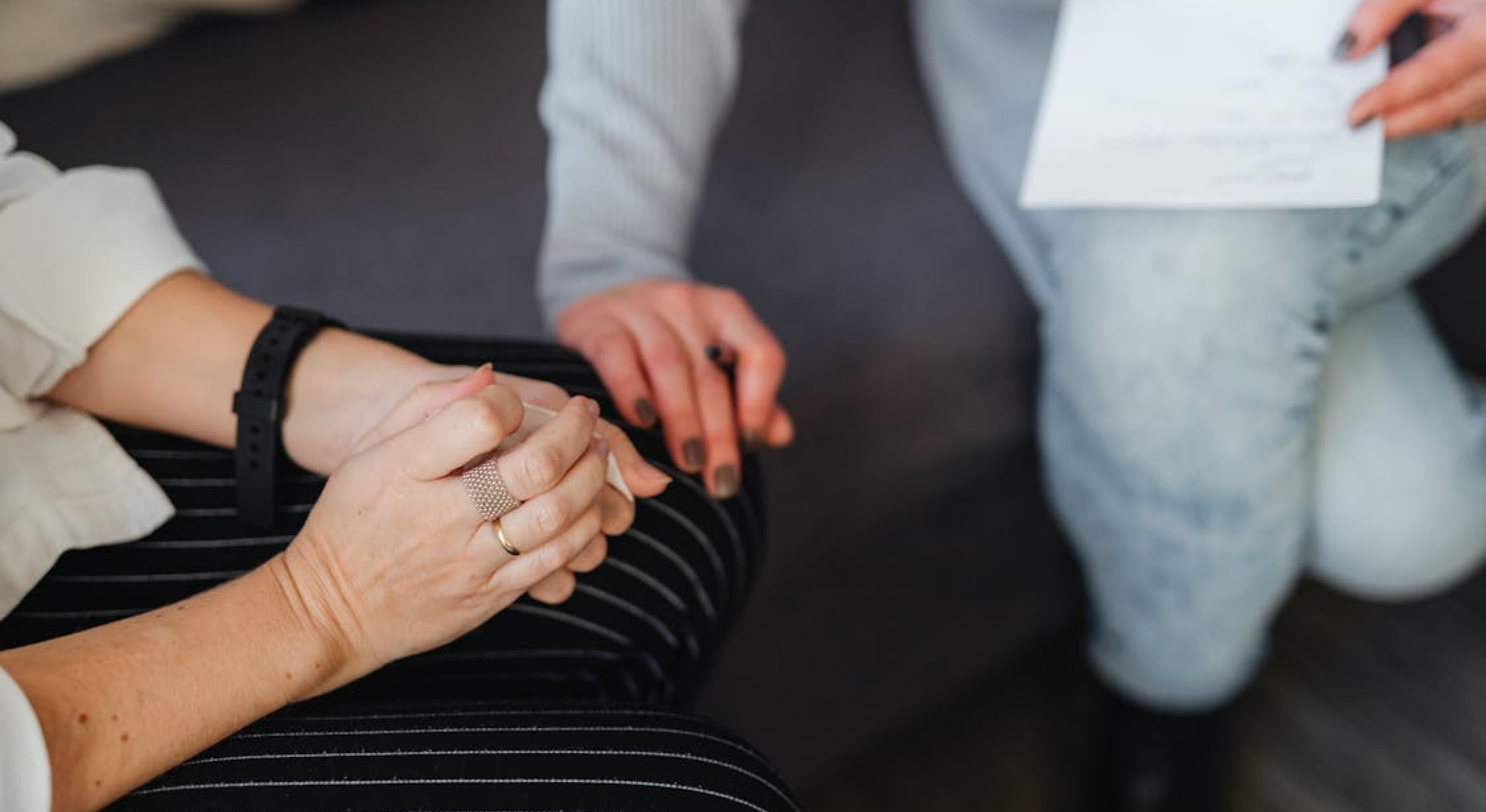 A person holds a white document while another clasps their hands.