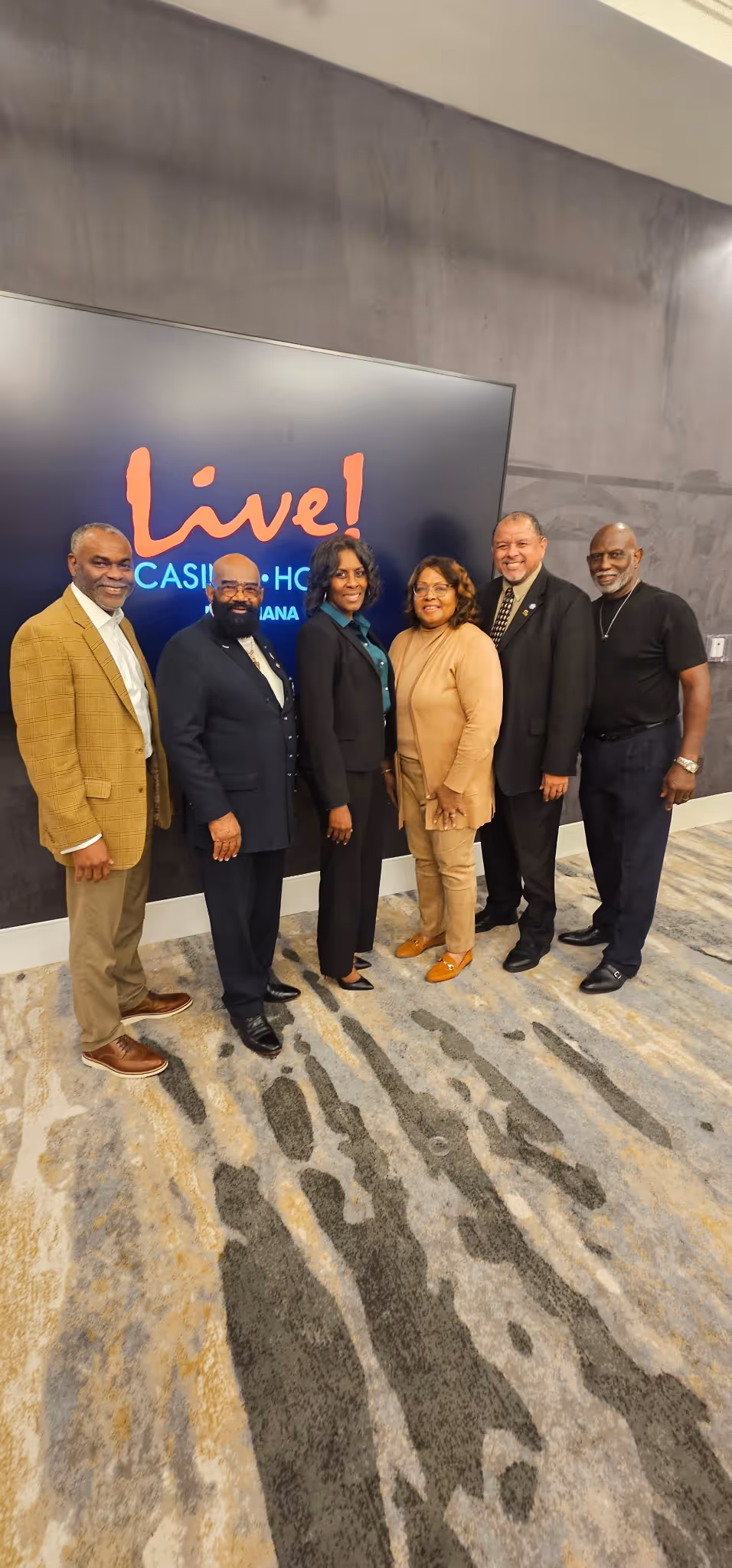 Six people standing indoors in front of a Live! Casino & Hotel Indiana sign, smiling and posing.