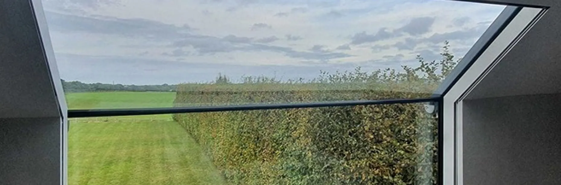 View of a green field and hedge seen through a modern triangular glass window.