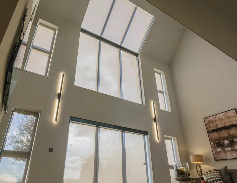 Interior view of tall sloped windows with vertical lights and a lamp beside a couch and painting.