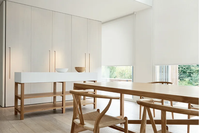 Modern dining room with wooden table, chairs, light wood cabinet, and bright windows with shades.