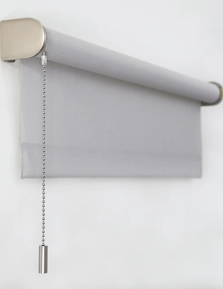 Light gray roller window blind with metal chain pull on a white wall.