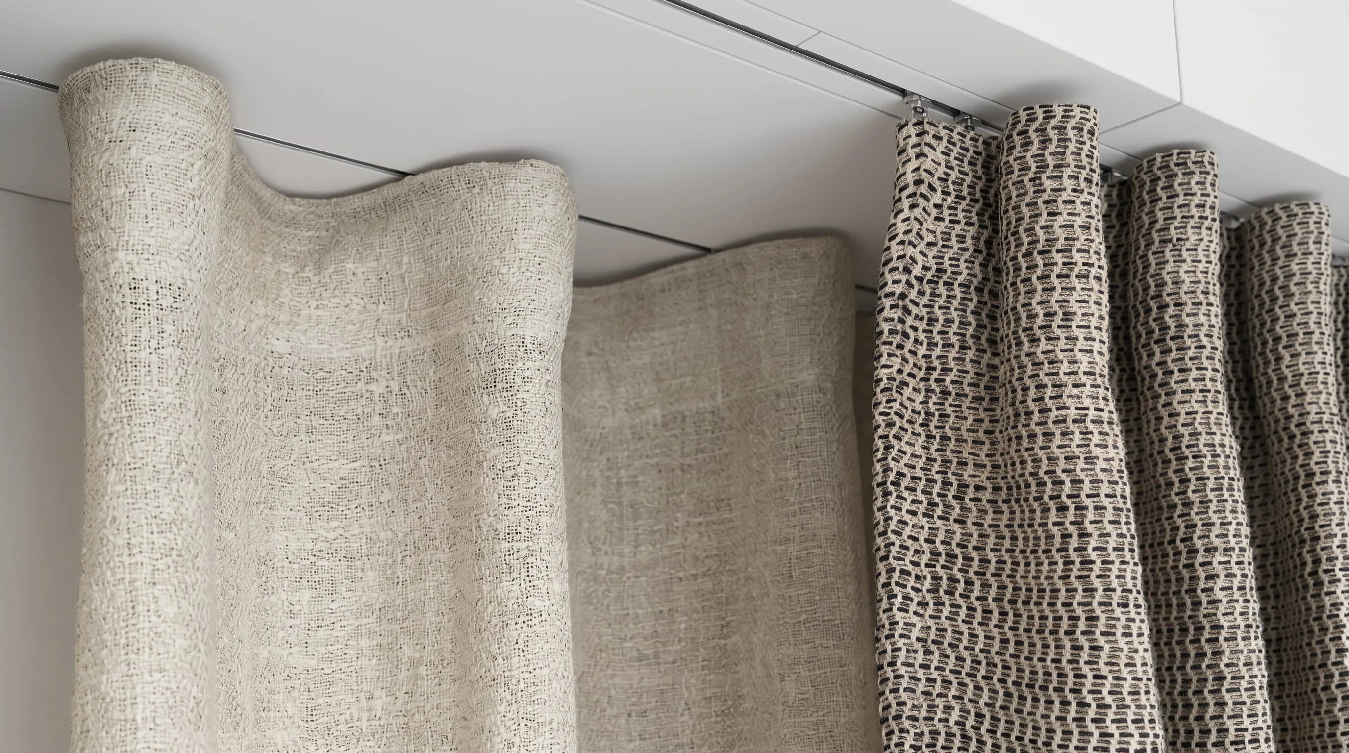 Close-up of beige and patterned curtains hanging from a white ceiling rail.
