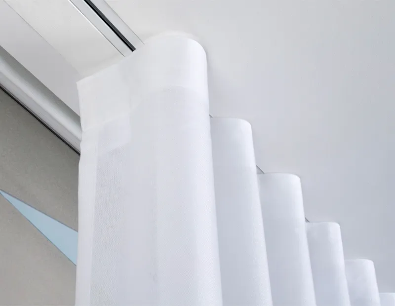 White sheer curtains hanging from a ceiling-mounted curtain track near a window.