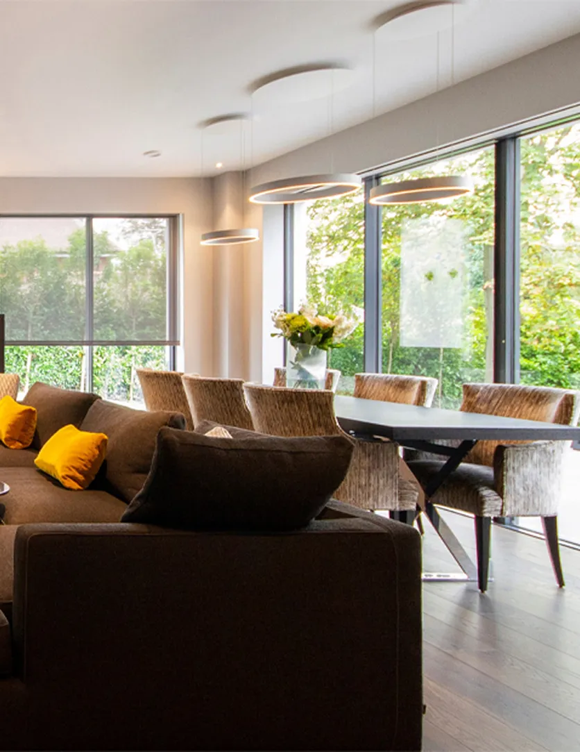 Modern dining area with large windows, round pendant lights, a dark table, and cushioned chairs.