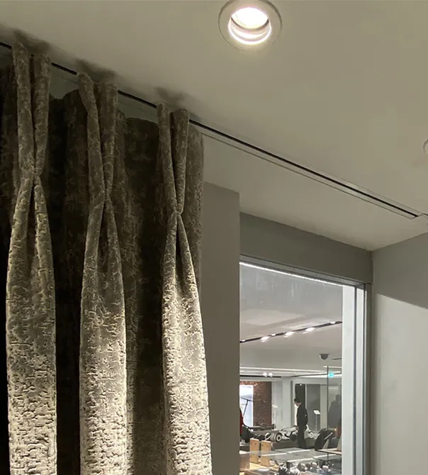 Thick beige curtains pulled to the side with a view into a well-lit room with people inside.