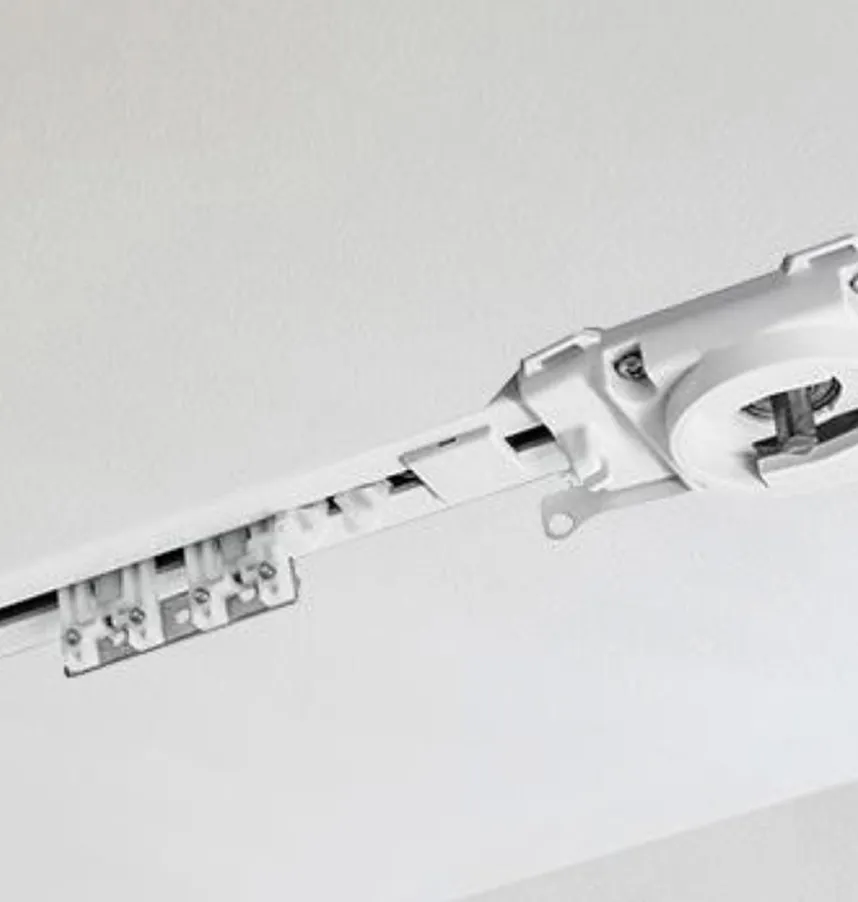 Close-up of a white curtain track mounted on a ceiling with rollers and a hook attachment.
