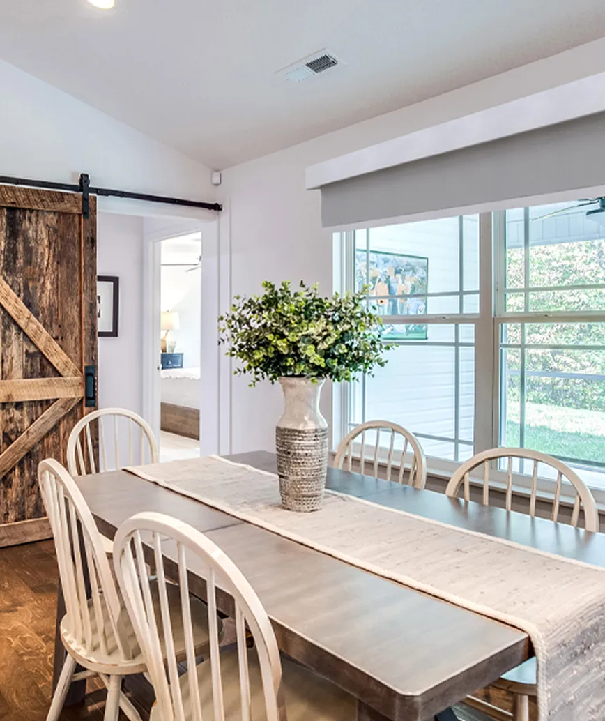 Dining room with wooden table, six white chairs, a vase with green foliage, and a rustic sliding barn door.