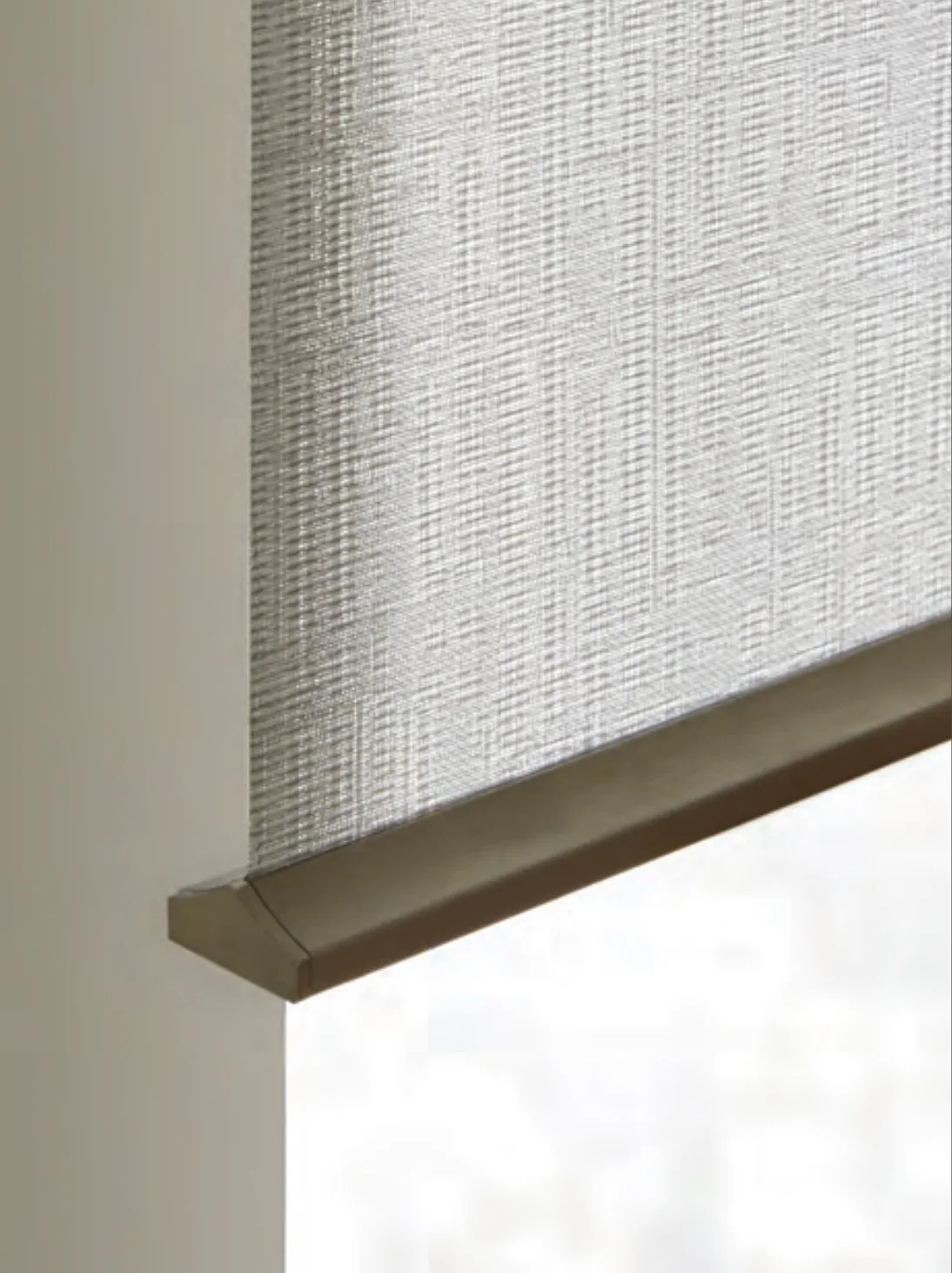 Close-up of a beige window roller shade with textured fabric partially lowered.