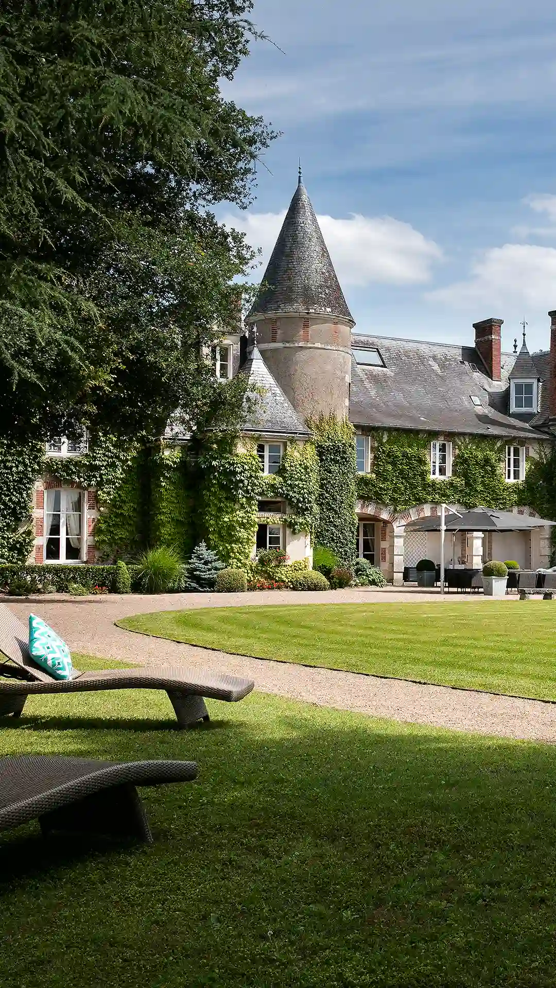 Teilansicht der Schlossfassade und des Turms, vom Rasen mit Liegestühlen aus gesehen. Seitenansicht des Hotels „Les Hauts de Loire“ – ein 5-Sterne-Hotel mit Restaurant und Spa.