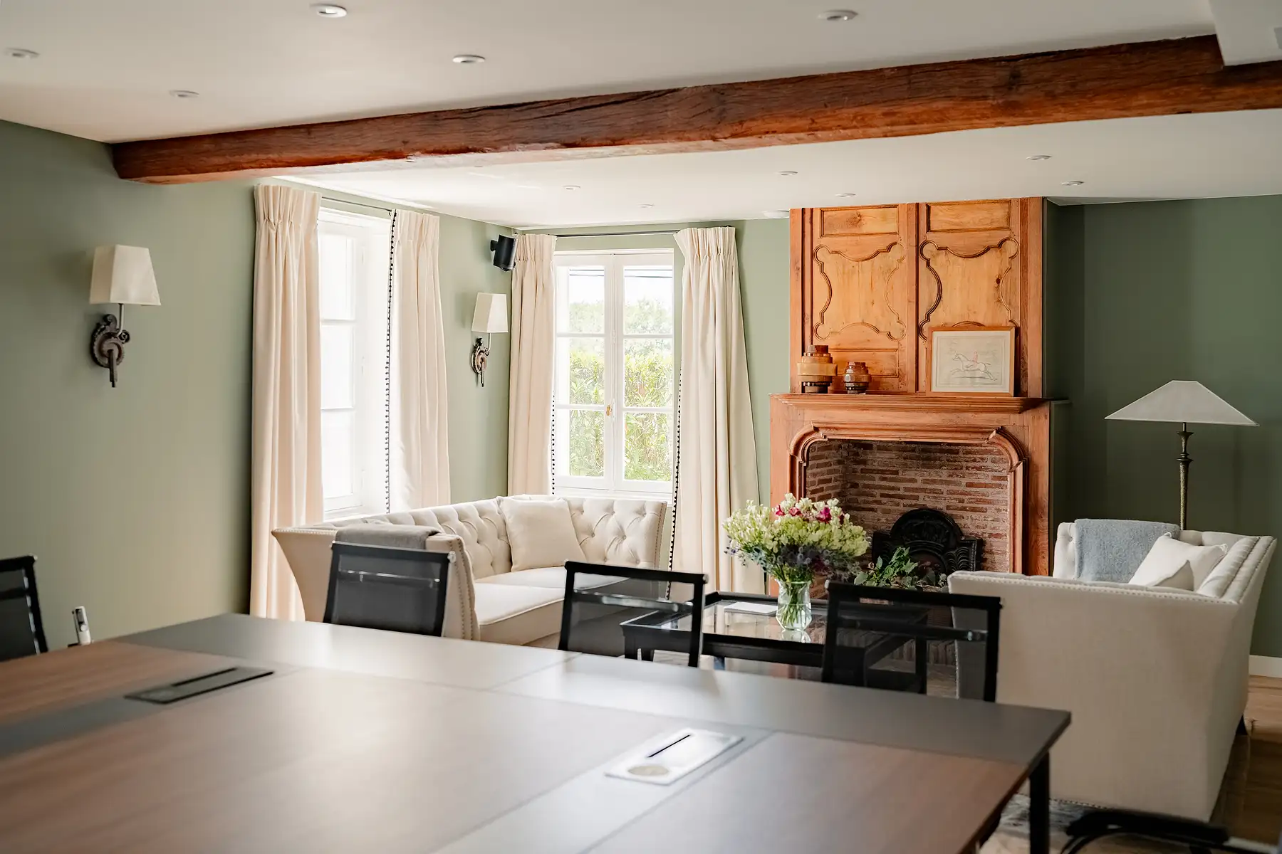 Besprechungsbereich mit Konferenztisch im Vordergrund und Sitzbereich mit Holzkamin im Hintergrund im Les Hauts de Loire – 5-Sterne-Hotel, Restaurant & Spa.