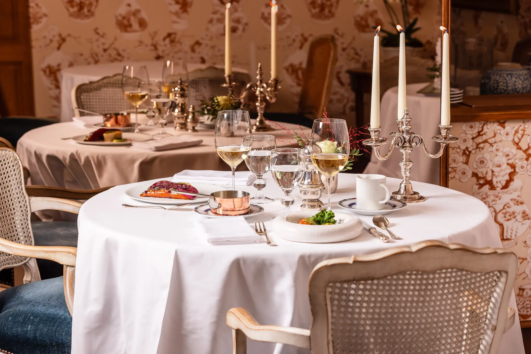 Gros plan sur deux tables dressées pour le repas avec nappes blanches, couverts et verres.