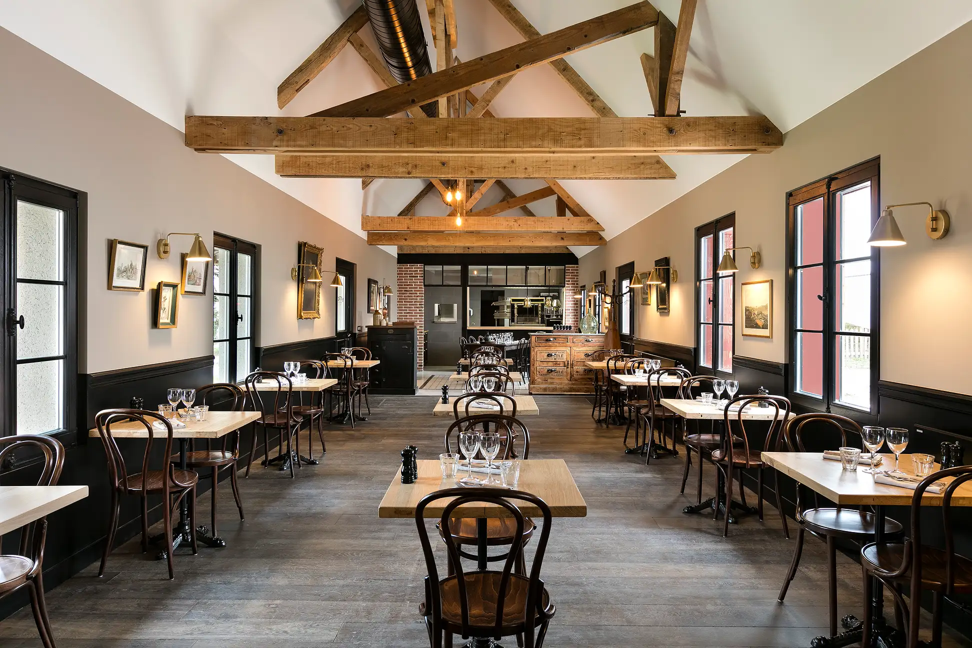 Salle de restaurant avec poutres apparentes, tables et chaises en bois, et murs décorés de cadres.