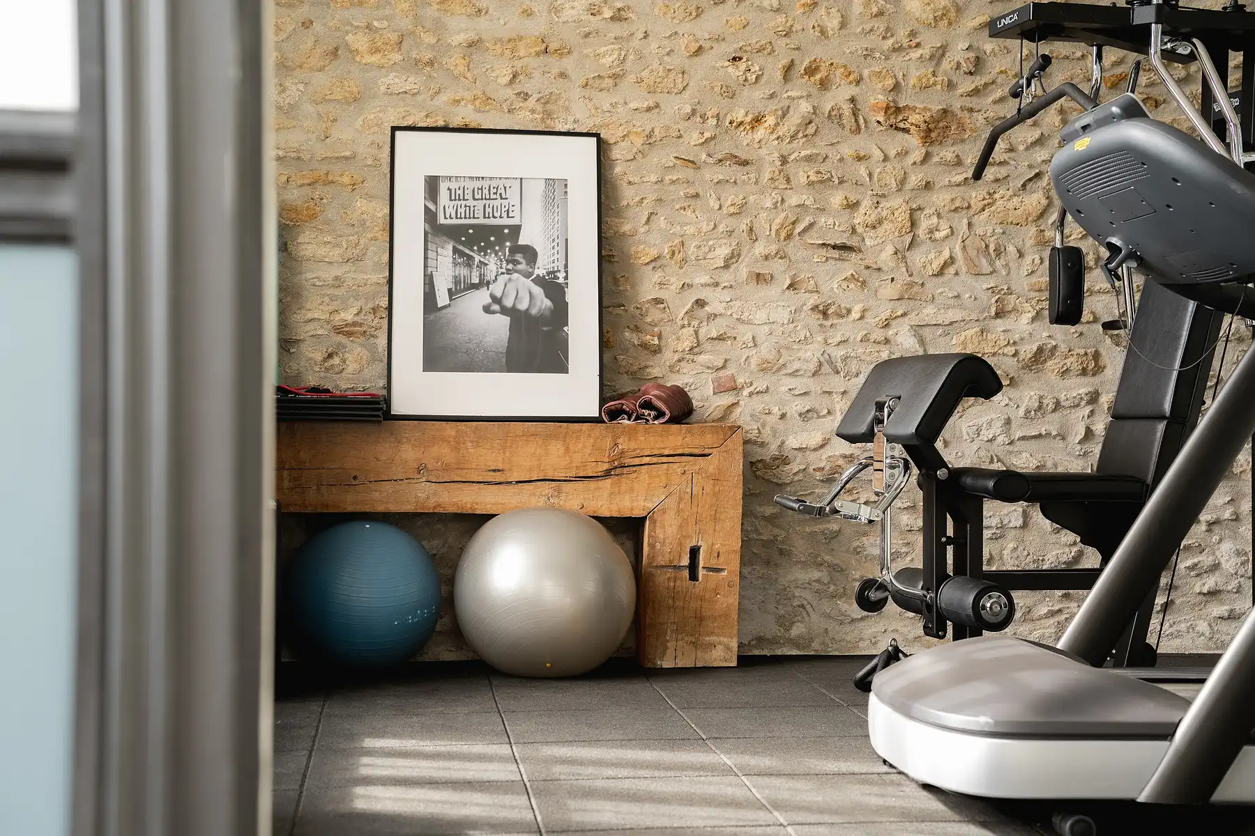 Hotel-Fitnessraum mit Laufband, Gymnastikbällen und einer Holzbank.