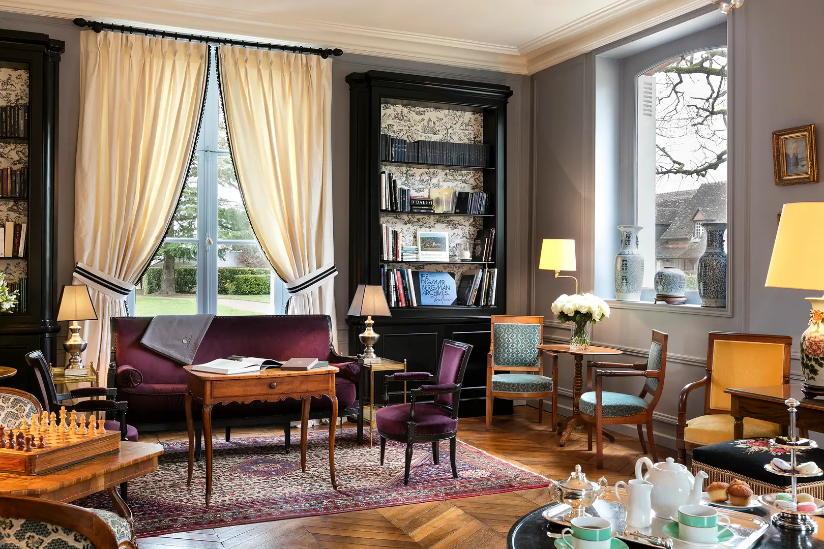 Eine weitere Ansicht des Wohnzimmers mit einem violetten Samtsofa, einem antiken Schreibtisch und verschiedenen Sesseln.