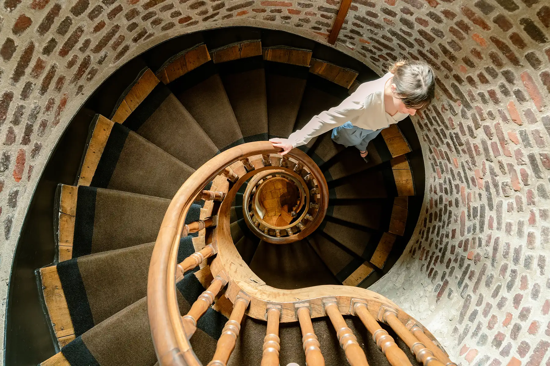 Ansicht von oben auf eine Person, die eine hölzerne Wendeltreppe in einem Steinturm hinaufsteigt.