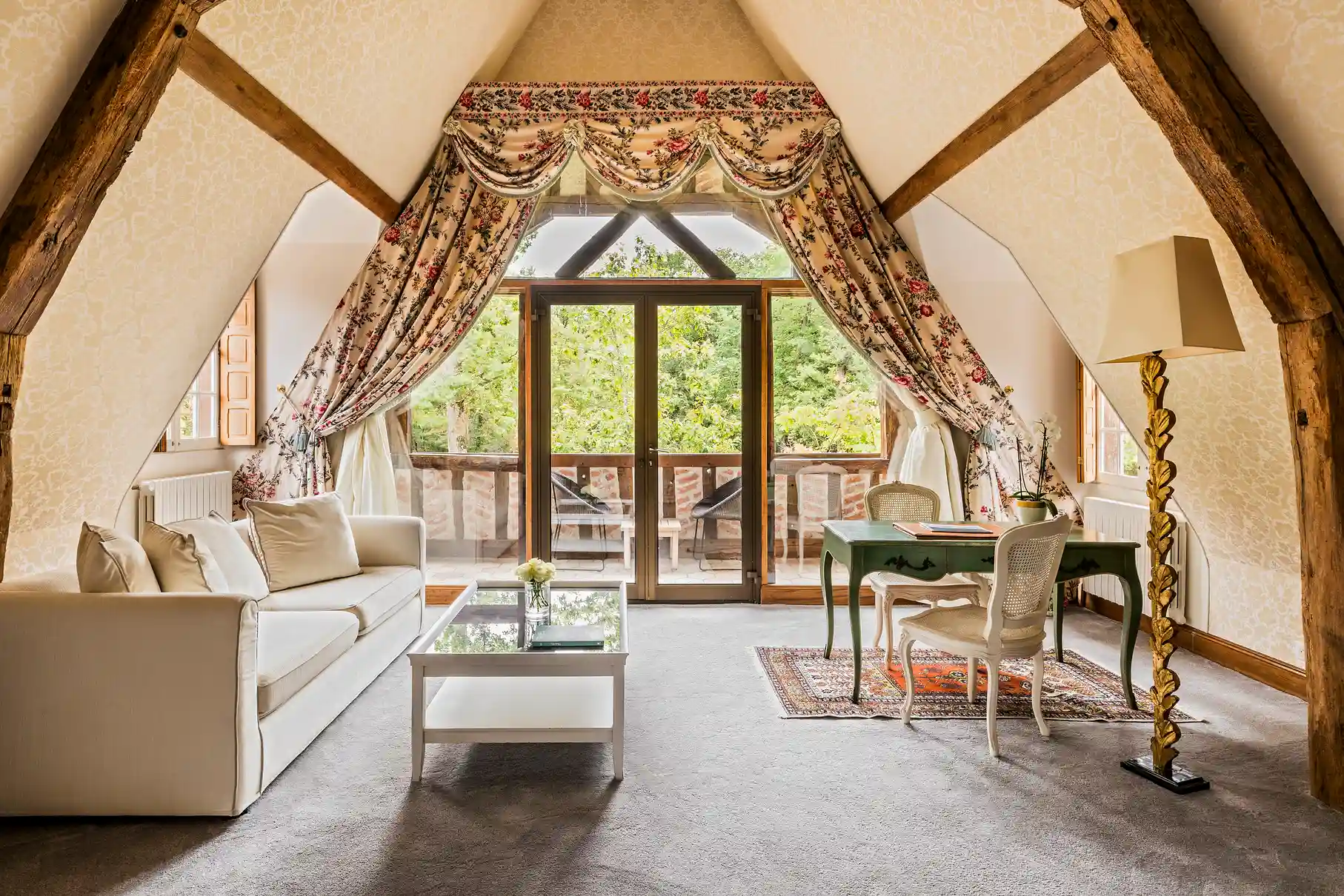 Suite mansardée de l'hôtel Les Hauts de Loire avec poutres apparentes, canapé blanc et vue sur le parc.