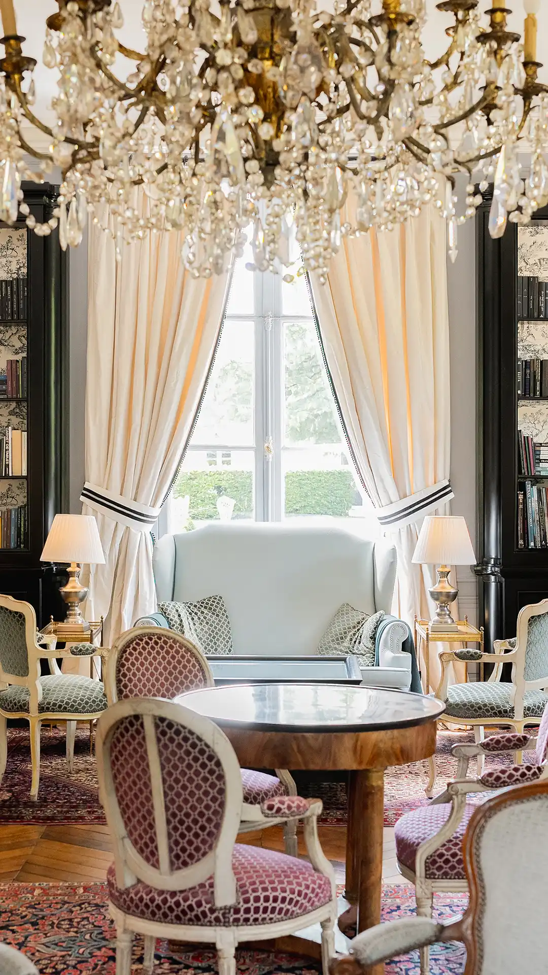 Le salon principal vu de face, mettant l'accent sur la symétrie de la fenêtre et des bibliothèques chez "Les Hauts de Loire – Hôtel, Restaurant & Spa – 5 étoiles".