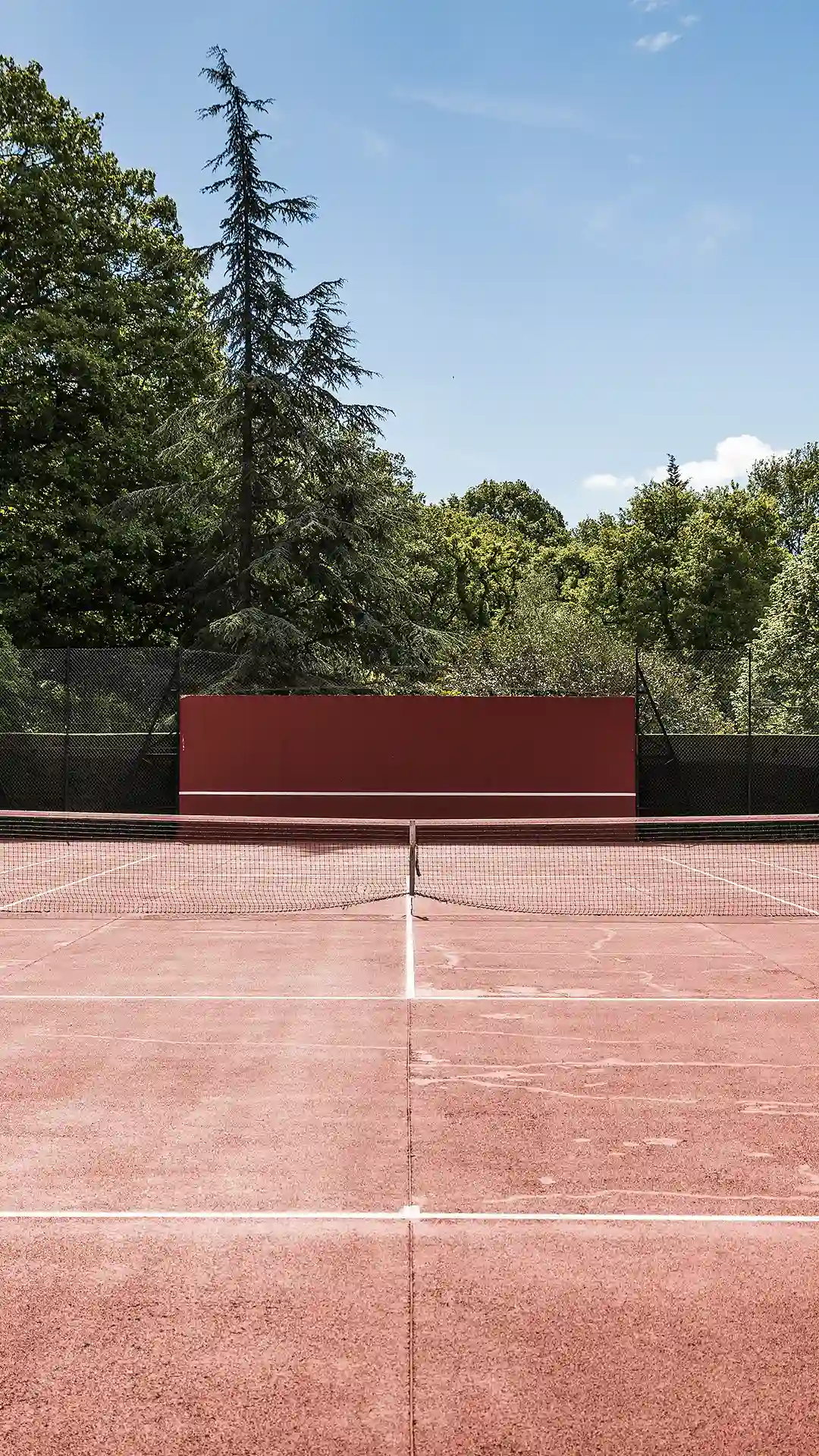 Gros plan sur le filet et la ligne médiane du court de tennis en terre battue, avec le mur rouge visible au fond. Les Hauts de Loire – Hôtel, Restaurant & Spa – 5 étoiles.