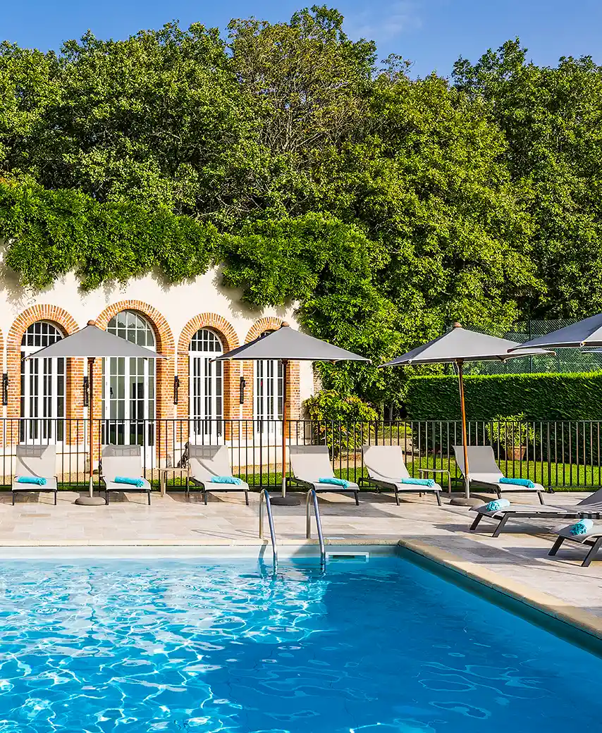 Vue ensoleillée de la piscine de l'hôtel Les Hauts de Loire – Hôtel, Restaurant & Spa – 5 étoiles, bordée de transats et parasols sous une façade couverte de vigne vierge.