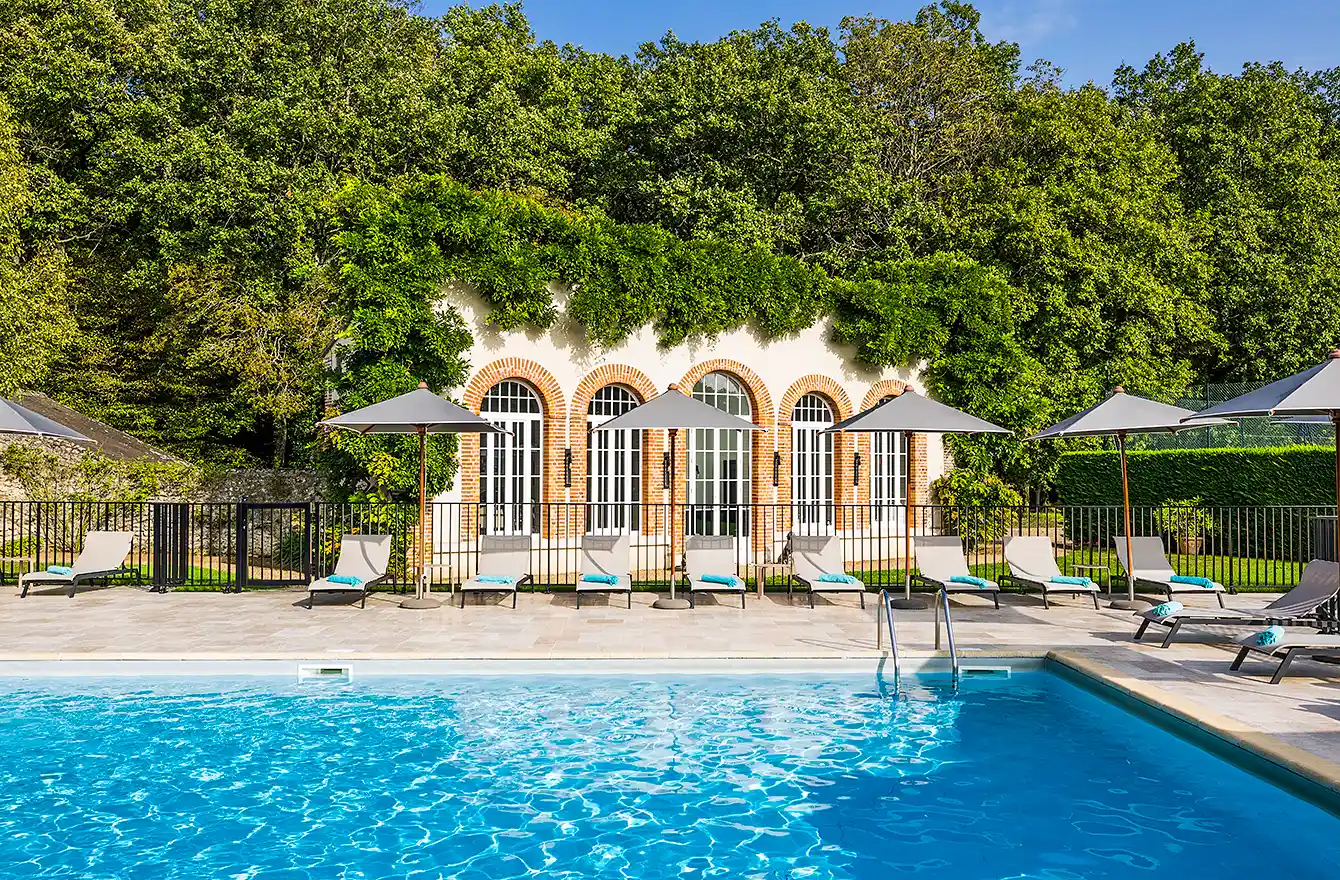 Scène de détente au bord de la piscine, montrant les détails des chaises longues et de la façade en pierre de l'hôtel Les Hauts de Loire – Hôtel, Restaurant & Spa – 5 étoiles.