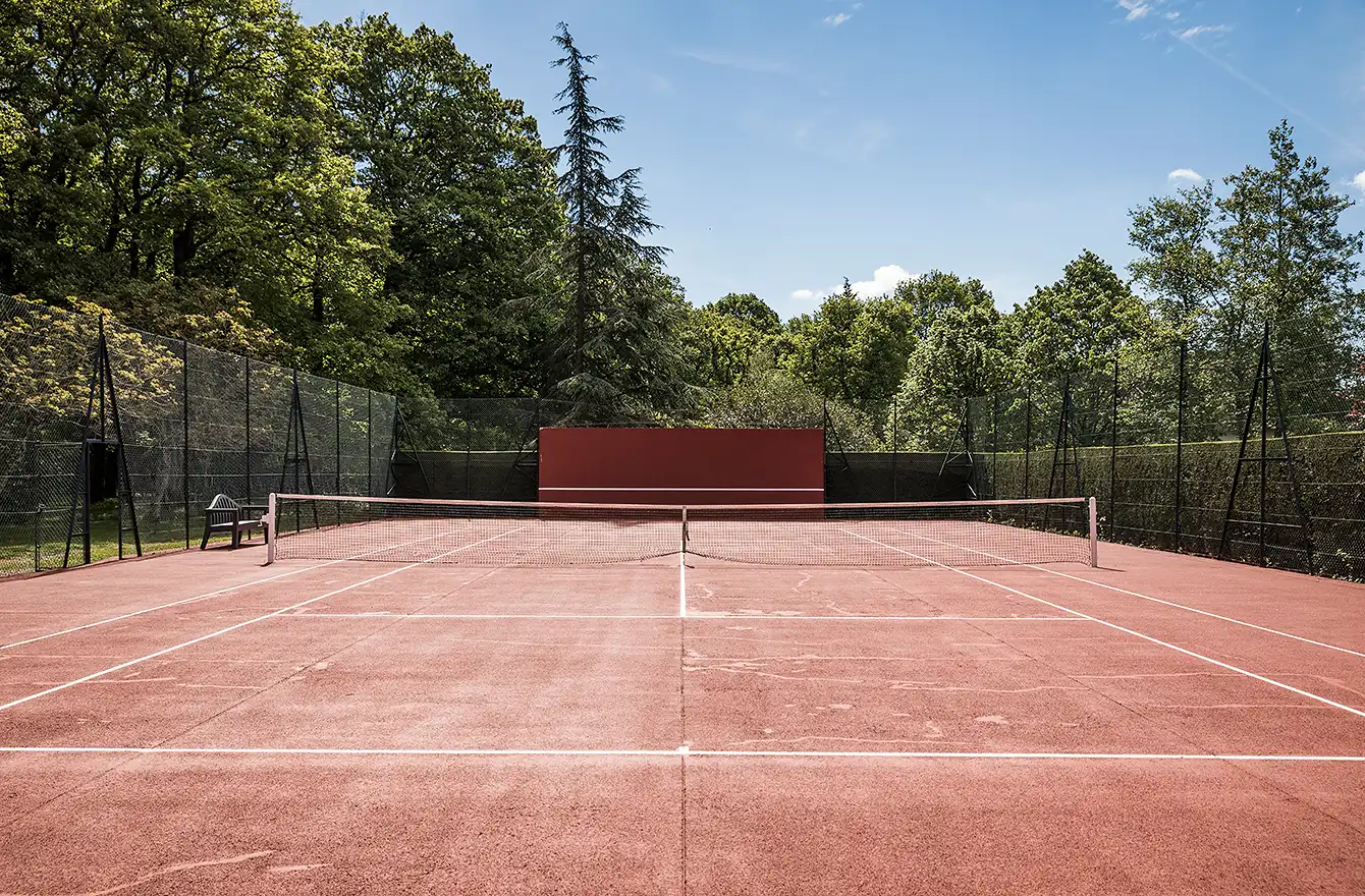 Vue depuis le fond du court de tennis en terre battue, montrant l'étendue du terrain vers le filet et le mur d'entraînement. Les Hauts de Loire – Hôtel, Restaurant & Spa – 5 étoiles.
